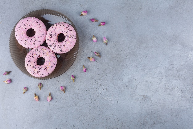 Three pink sweet donuts with budding roses on glass plate. 