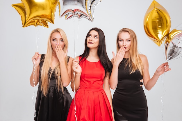 Three playful pretty young women standing and holding star shaped balloons over white background