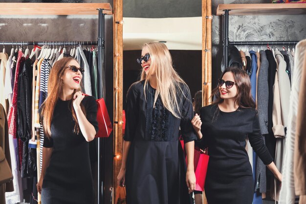 Three pretty smiling girls doing shopping in the fashion luxury shop on black friday sale