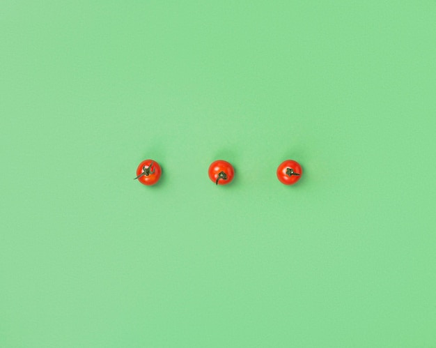 Three red cherry tomatoes on a green background top view minimalism