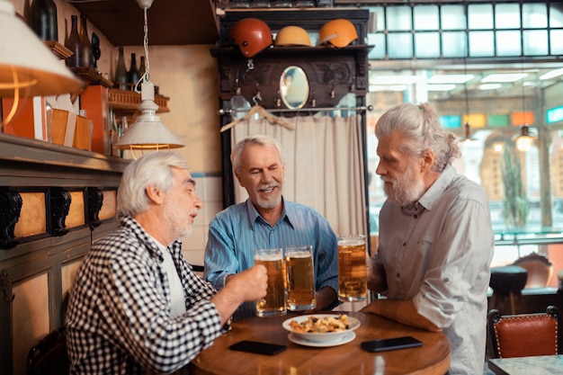 Three retired men. Three grey-haired aged retired men eating snacks and drinking beer