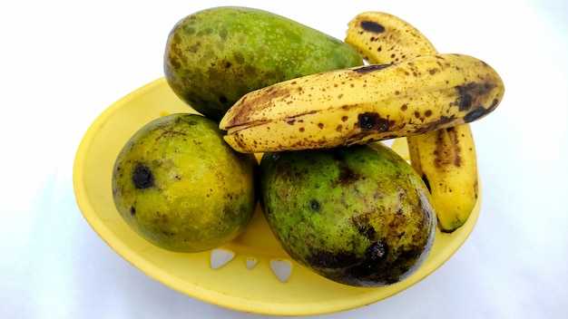 Three ripe mangoes and bananas in a basket isolated on white background