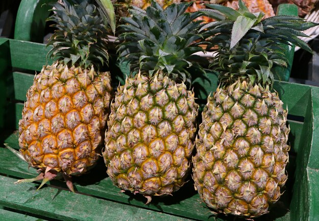 Three Ripe Pineapple Whole Fruits with Green Stem in a Wooden Basket, Thailand                    