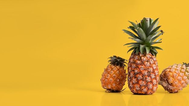 Photo three ripe pineapples against yellow background summer vacation beach copy space