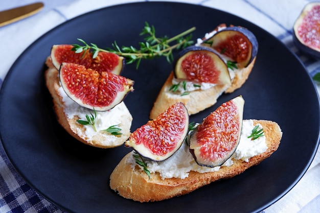 Three sandwiches with goat cheese, fig and thyme served on a black plate on light grey surface