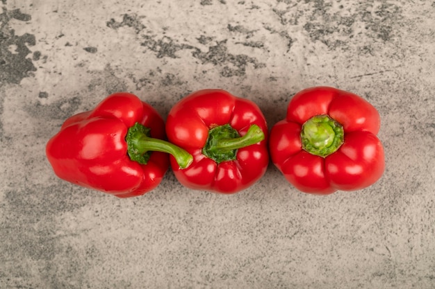 Three shiny red bell peppers on stone surface