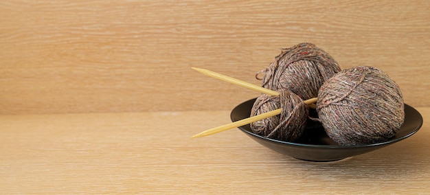 three skeins of brown rustic wool with wooden spokes in a black plate on a wooden surface