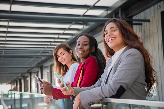 Three smiling corporate businesswomen working with smart phones and looking at camera diversity