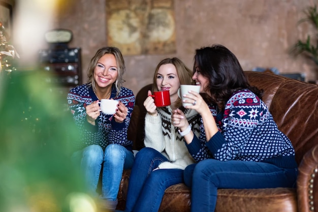 Three smiling women talking and drinking coffee while sitting on a couch