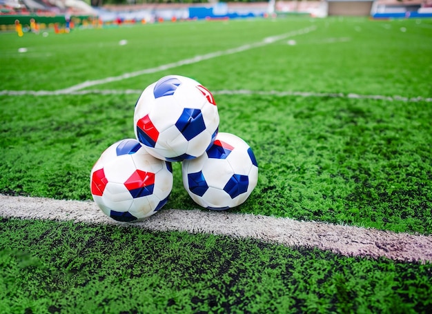 Three soccer balls are stacked on a green field.