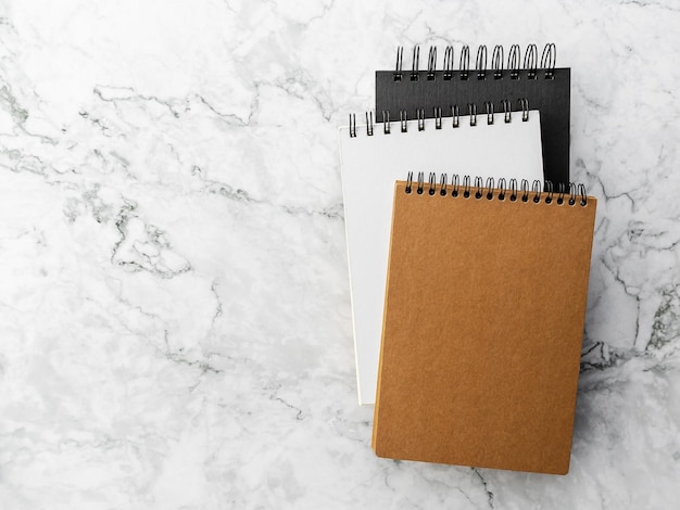 Three spiral notebook black white and brown in hard covers on a gray marble background