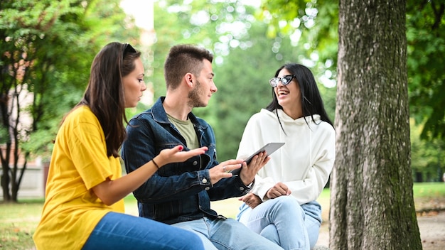 Three students studying together with a digital tablet sitting on a bench outdoor