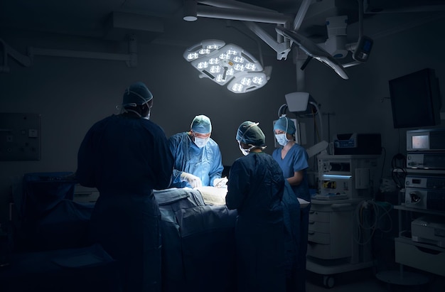 Photo three surgeons in a hospital room one of which is being prepared to perform surgery