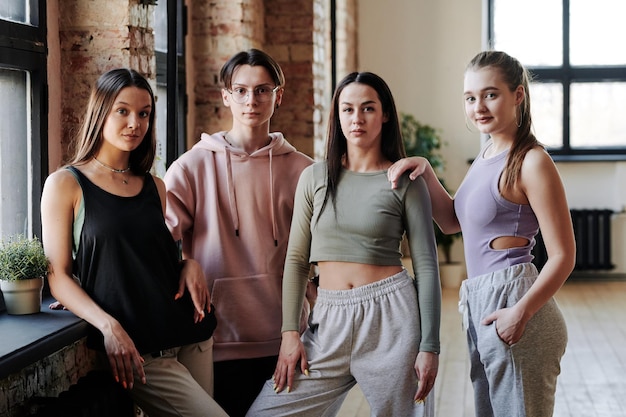 Three teenage girls and guy in activewear standing in modern loft studio