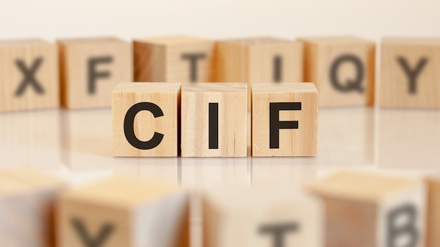 Three toy wood blocks with letters CIF on a table with light background, selective focus. CIF - short for cost insurance and freight