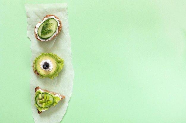 Photo three vegetarian sandwiches on parchment paper piece on green background