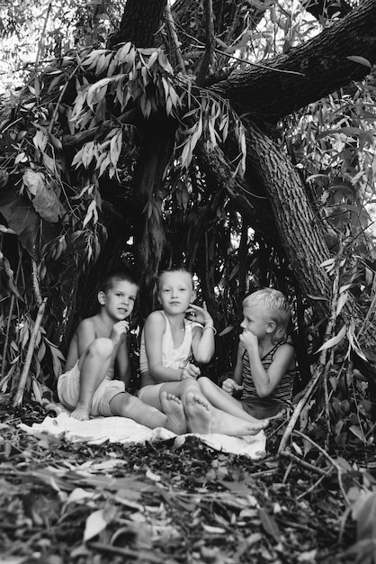 Three village children are playing in a hut which they themselves have built from leaves and twigs Wooden house in the forest Black and white photography