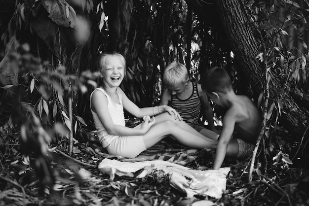 Three village children are playing in a hut which they themselves have built from leaves and twigs Wooden house in the forest Black and white photography