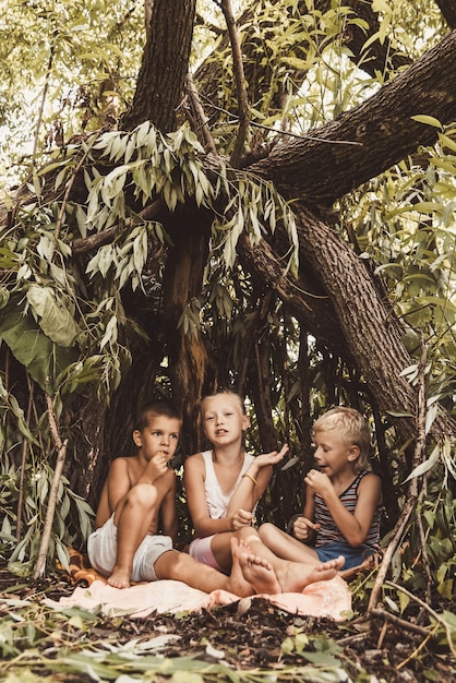 Three village children are playing in a hut which they themselves have built from leaves and twigs