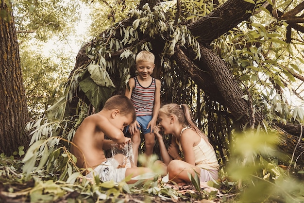 Three village children are playing in a hut which they themselves have built from leaves and twigs