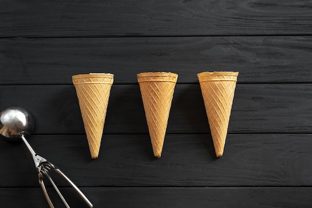 Three waffle cups for ice cream empty on a black wooden background view from above next to the ice c