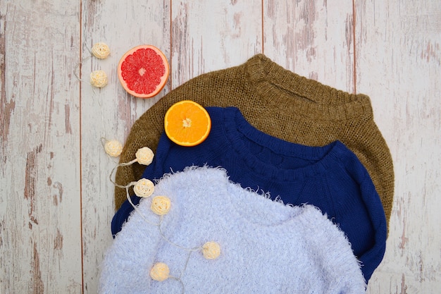 Three warm sweater on a wooden . Garland, orange and grapefruit. Fashionable , top view