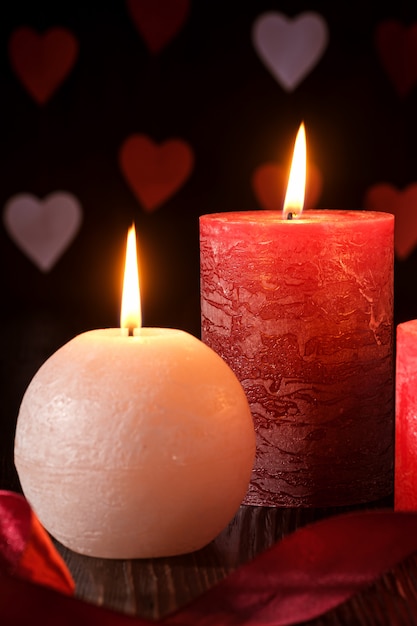 Three wax flame candlelight with ribbon in dark romantic light on hearts