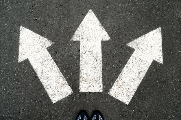 Three white arrows pointing in different directions on gray asphalt 