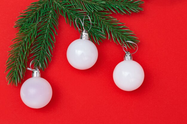 Three White christmas glass balls on green branches over red background