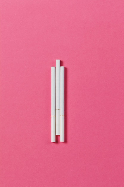 Three white cigarettes on pink rose background