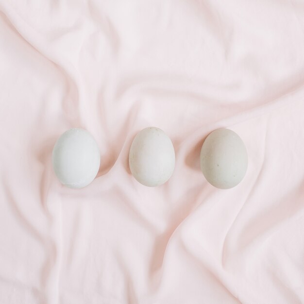 Three white Easter eggs on pink textile surface