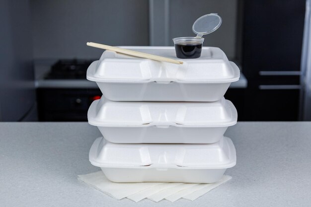 Three white food containers are on the kitchen table Chopsticks for eating sushi and a box of soy sauce