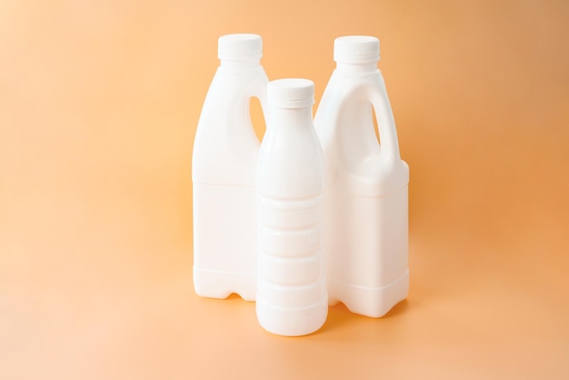 Three white plastic bottles for milk on orange background Mock up Blank Natural Pasteurized Fat Nutrient Design Mock Beverage Diet Fresh Liquid Empty Lid Gallon Grocery Daily