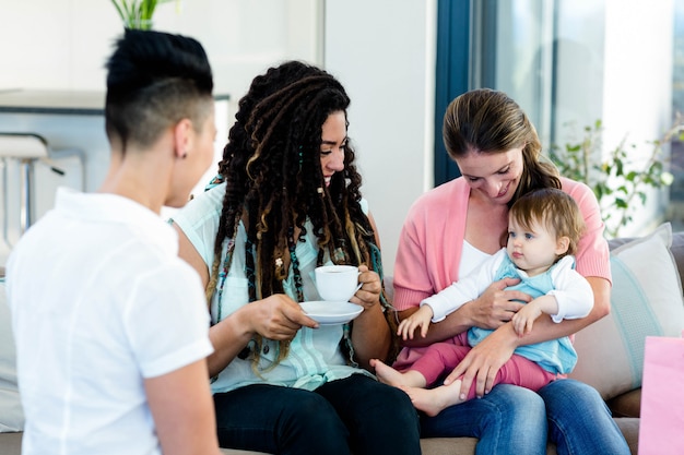 Three woman smiling and sitting on sofa with a baby