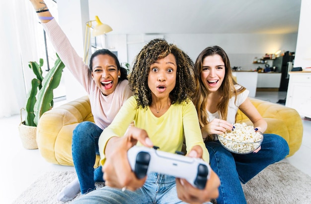 Three women playing video games sitting on sofa at home