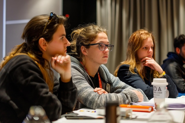 Photo three women sit at a table with one wearing glasses and one has a gray sweater on it