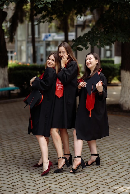 Photo three women wearing black dresses and red scarfs stand on a sidewalk