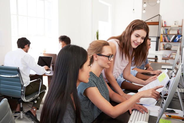 Three women working together at computer in open plan office