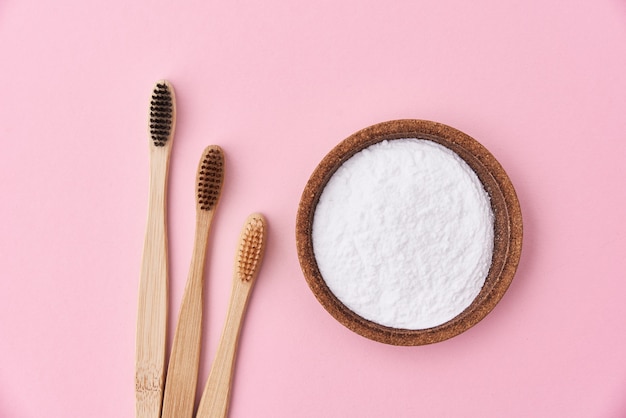 Three wooden bamboo toothbrushes and baking soda, top view