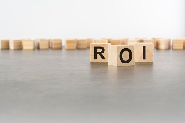 Three wooden blocks with letters ROI with focus to the single cube in the foreground in a conceptual image on grey background