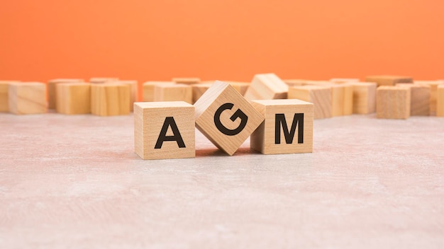 Three wooden cubes with the letters AGM on gray surface orange background