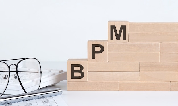 Three wooden cubes with letters BPM Business Process Management on the white table with keyboard and glasses