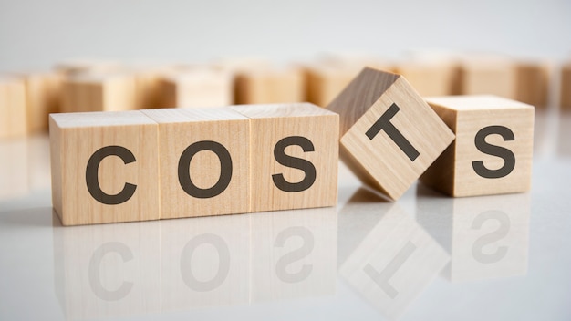 Three wooden cubes with the letters Costs on the bright surface of a gray table. the inscription on the cubes is reflected from the surface of the table. business concept