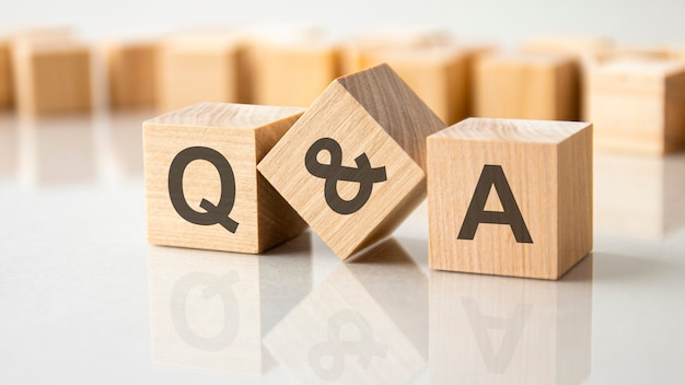 Three wooden cubes with the letters Q and A on the bright surface of a gray table, business concept