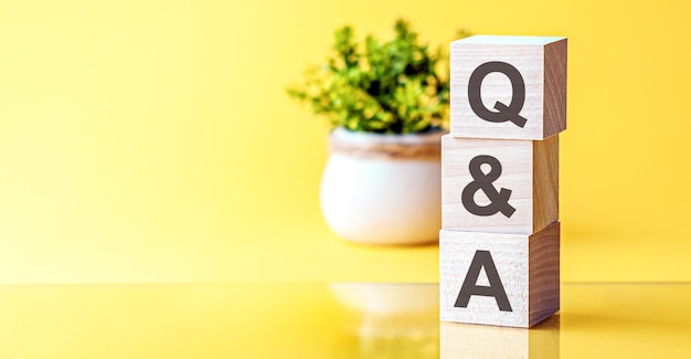 Three wooden cubes with letters - q and a - question and answer, on yellow table, space for text in left. Front view concepts, flower in the background.