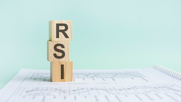 Three wooden cubes with letters RSI - means Relative Strength Index, on white table and diagram, business concept