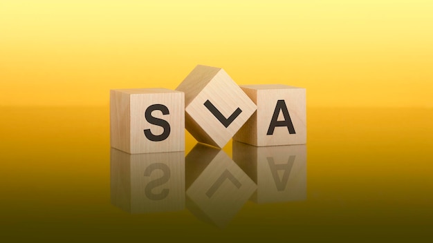 Three wooden cubes with the letters SLA on the bright yellow surface the inscription on the cubes is reflected from the gray surface of the table SLA short for Service Level Agreement