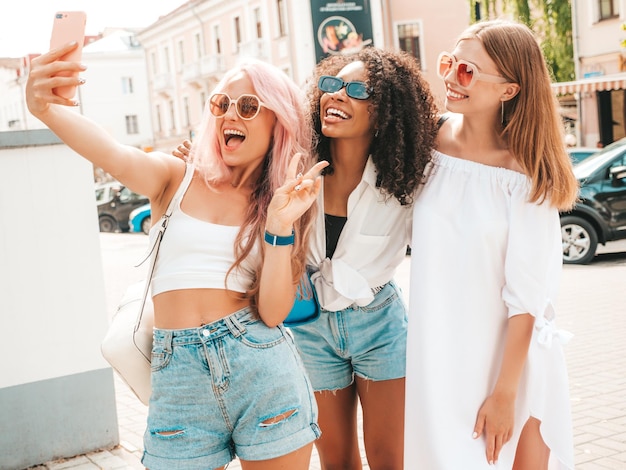 Three young beautiful smiling female in trendy summer clothesSexy carefree multiracial women posing on the street backgroundPositive models having fun in sunglasses Cheerful and happy