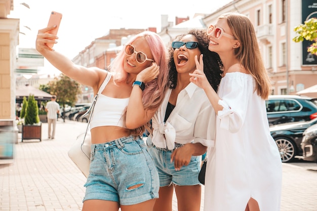 Three young beautiful smiling female in trendy summer clothesSexy carefree multiracial women posing on the street backgroundPositive models having fun in sunglasses Cheerful and happy