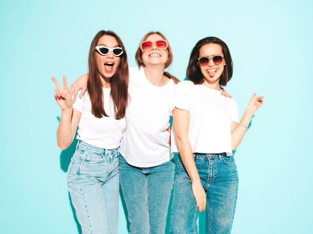 Three young beautiful smiling hipster female in trendy same summer white t-shirt and jeans clothes